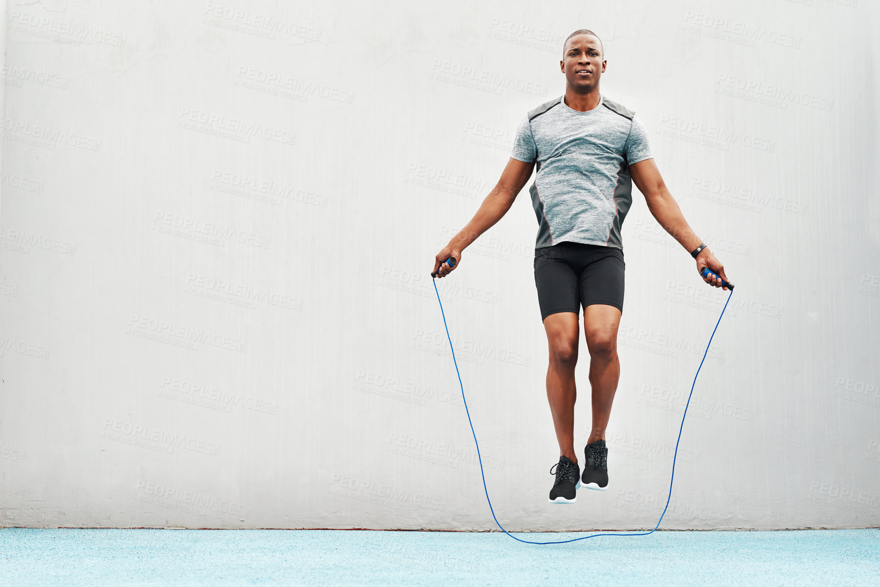 Buy stock photo Jump, rope and training with black man skipping in stadium for sports, workout practice and cardio. Health and body with athlete jumping on track for strong, mockup space and exercise against wall