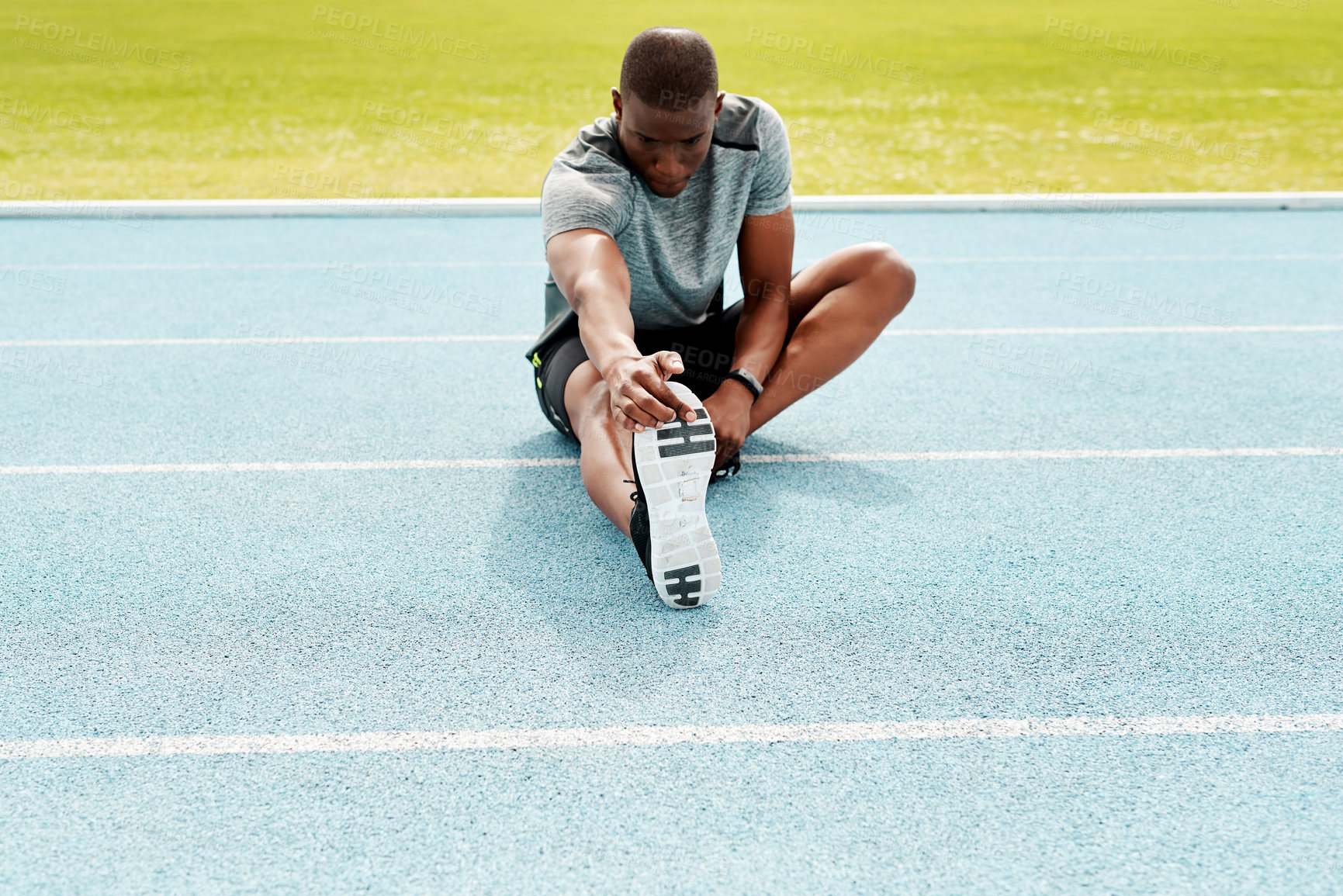 Buy stock photo Athlete man, sitting and track for stretching legs to start training, exercise or running for fitness outdoor. African runner, warm up muscle or body for workout at stadium for race, contest or sport