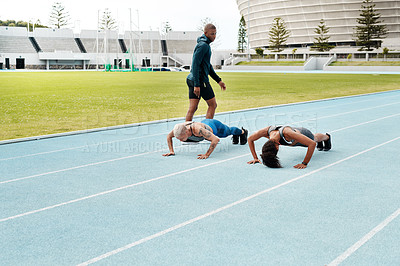 Buy stock photo Full length shot of two attractive young athletes doing press-ups on a track field while their coach watches