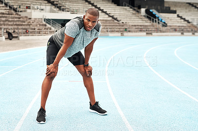 Buy stock photo Full length portrait of a handsome young athlete standing on a track field alone and catching his breath after running