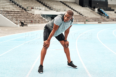 Buy stock photo Full length shot of a handsome young athlete standing on a track field alone and catching his breath after running