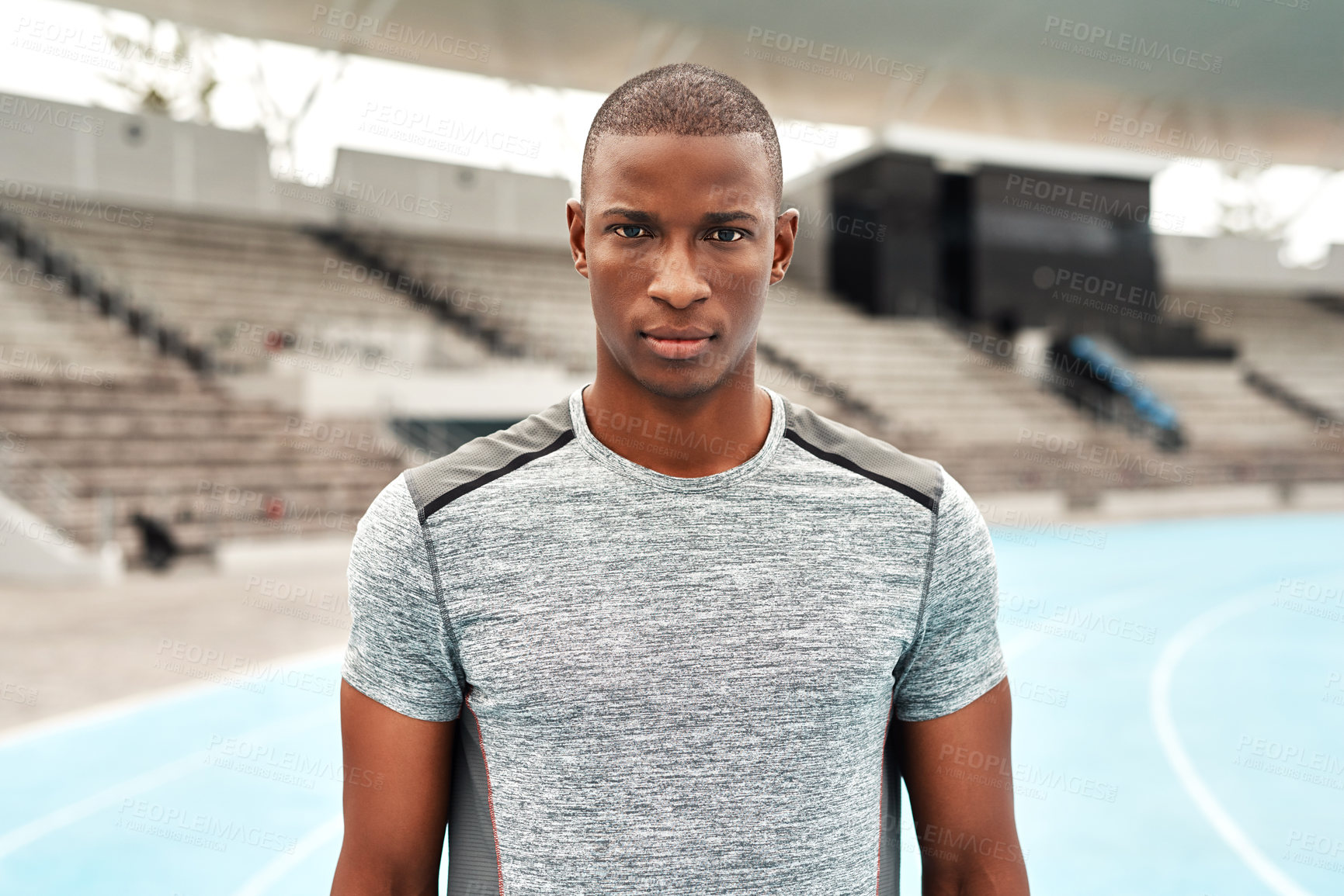 Buy stock photo Cropped portrait of a handsome young athlete standing alone before going for a run on a track field