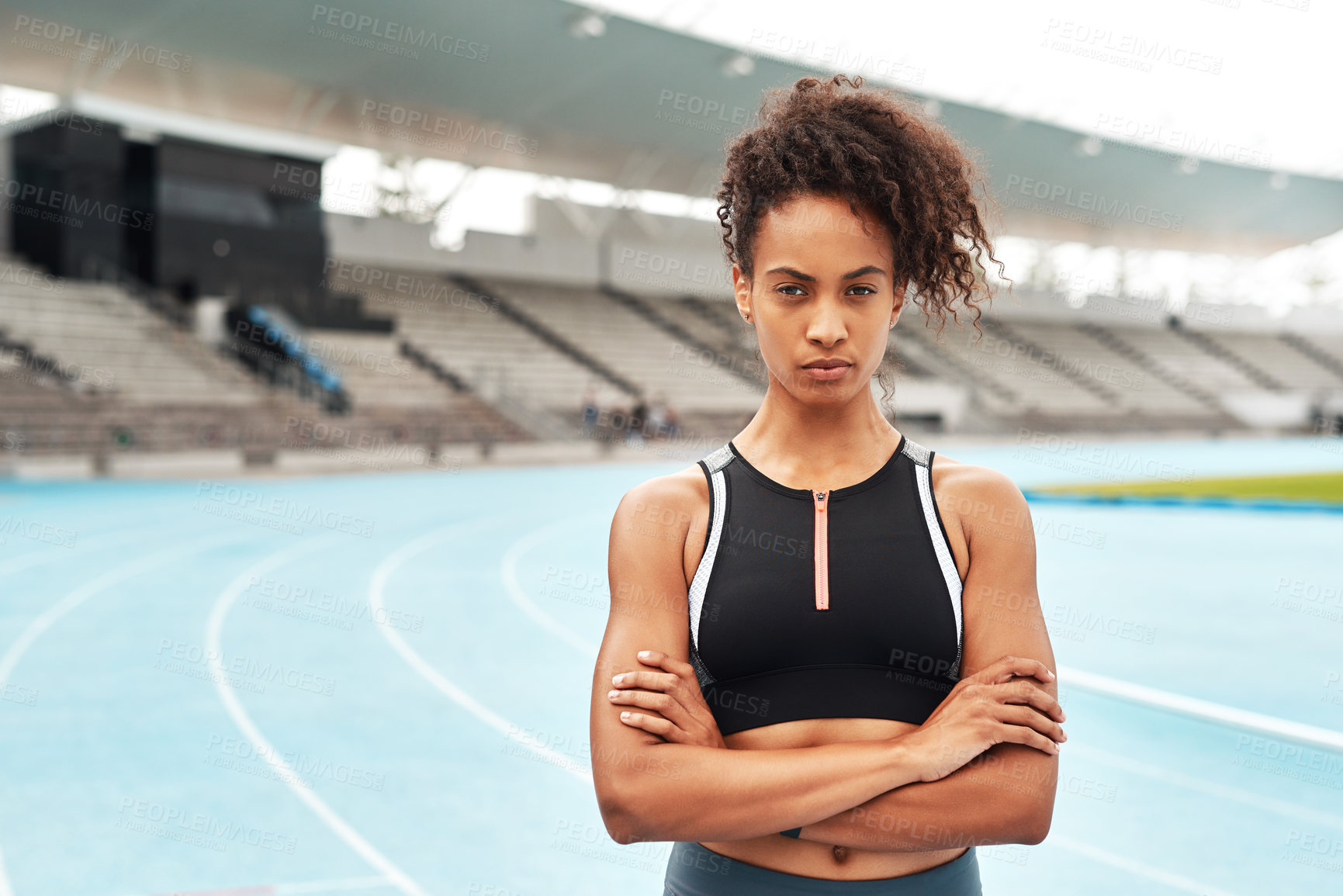 Buy stock photo Cropped portrait of an attractive young athlete standing alone with her arms folded before running a track field
