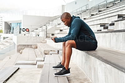 Buy stock photo Full length shot of a handsome young athlete sitting alone and texting on his cellphone after an outdoor training session