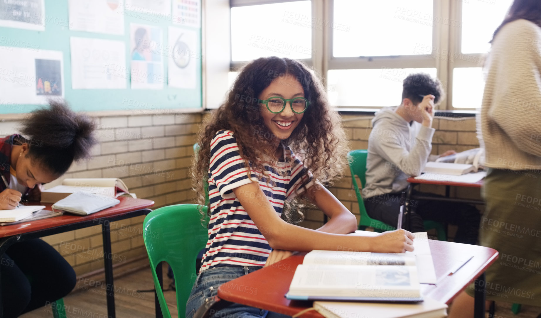 Buy stock photo Portrait of a cheerful young school kid seated at her desk while doing work inside of a classroom at school