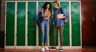 Buy stock photo Cropped shot of two young school kids browsing on a cellphone together while waiting to go to class inside of a school