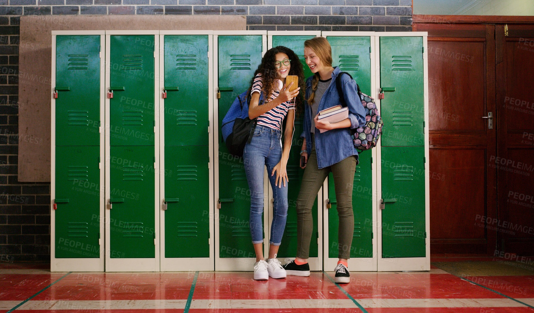 Buy stock photo Cropped shot of two young school kids browsing on a cellphone together while waiting to go to class inside of a school