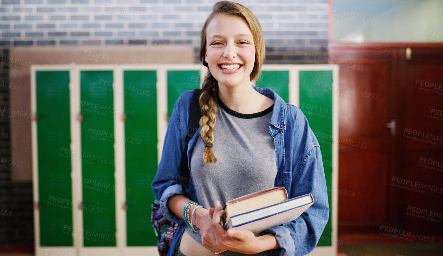 Buy stock photo Cropped shot of a cheerful young school kid holding her books while waiting to go to class inside of a school during the day