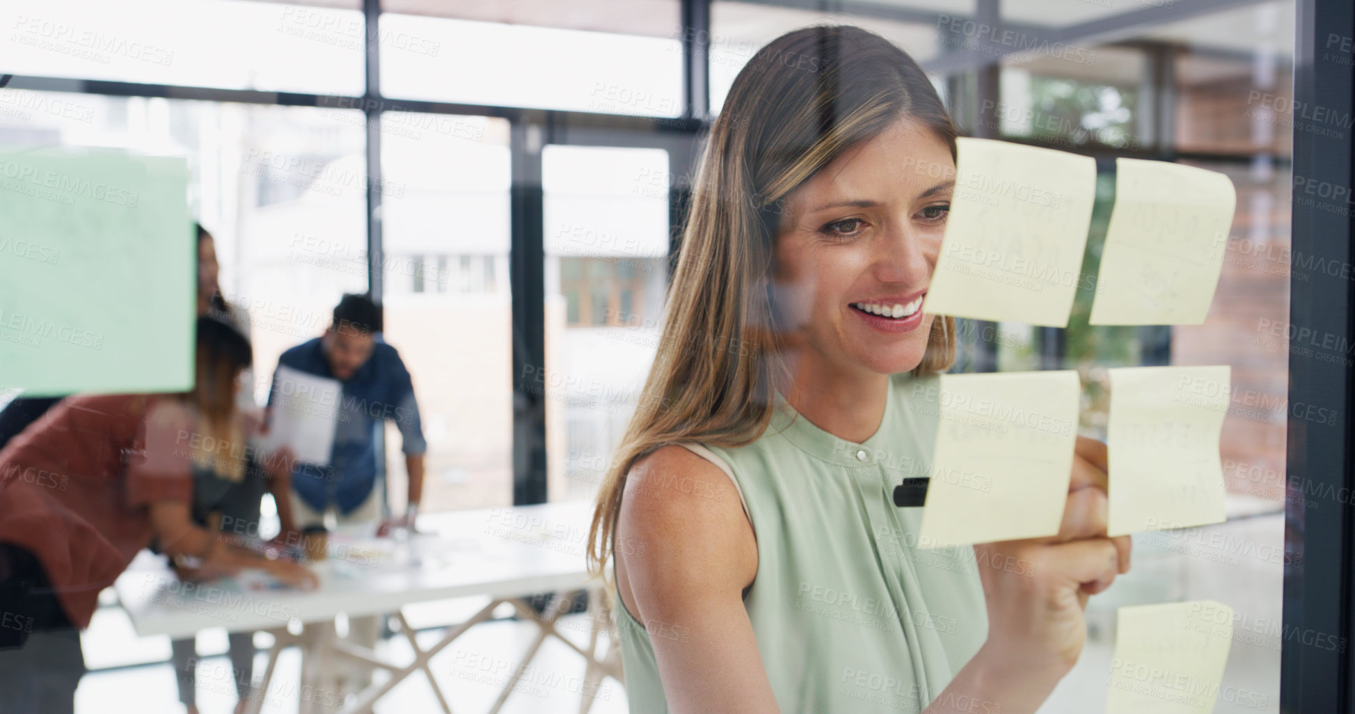 Buy stock photo Shot of a young businesswoman brainstorming with notes on a glass wall in an office