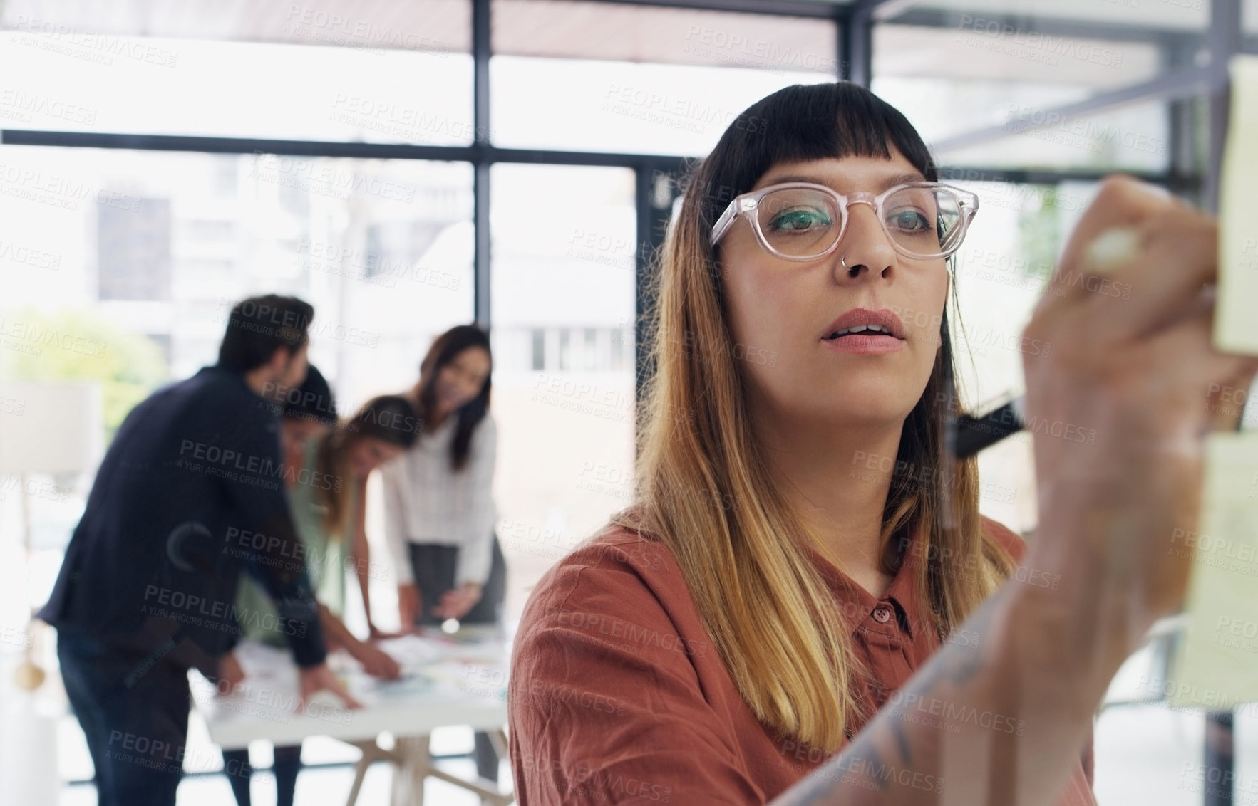 Buy stock photo Shot of a young businesswoman brainstorming with notes on a glass wall in an office