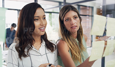 Buy stock photo Shot of two businesswomen brainstorming with notes on a glass wall in an office