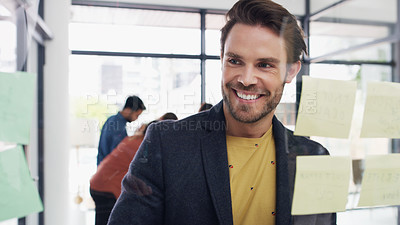 Buy stock photo Shot of a young businessman brainstorming with notes on a glass wall in an office