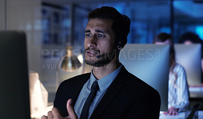 Buy stock photo Cropped shot of a handsome young businessman wearing a headset and sitting in the office late at night