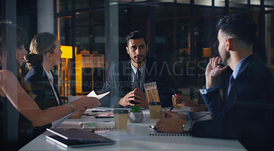 Buy stock photo Cropped shot of a diverse group of businesspeople sitting together and having a meeting in the office late at night