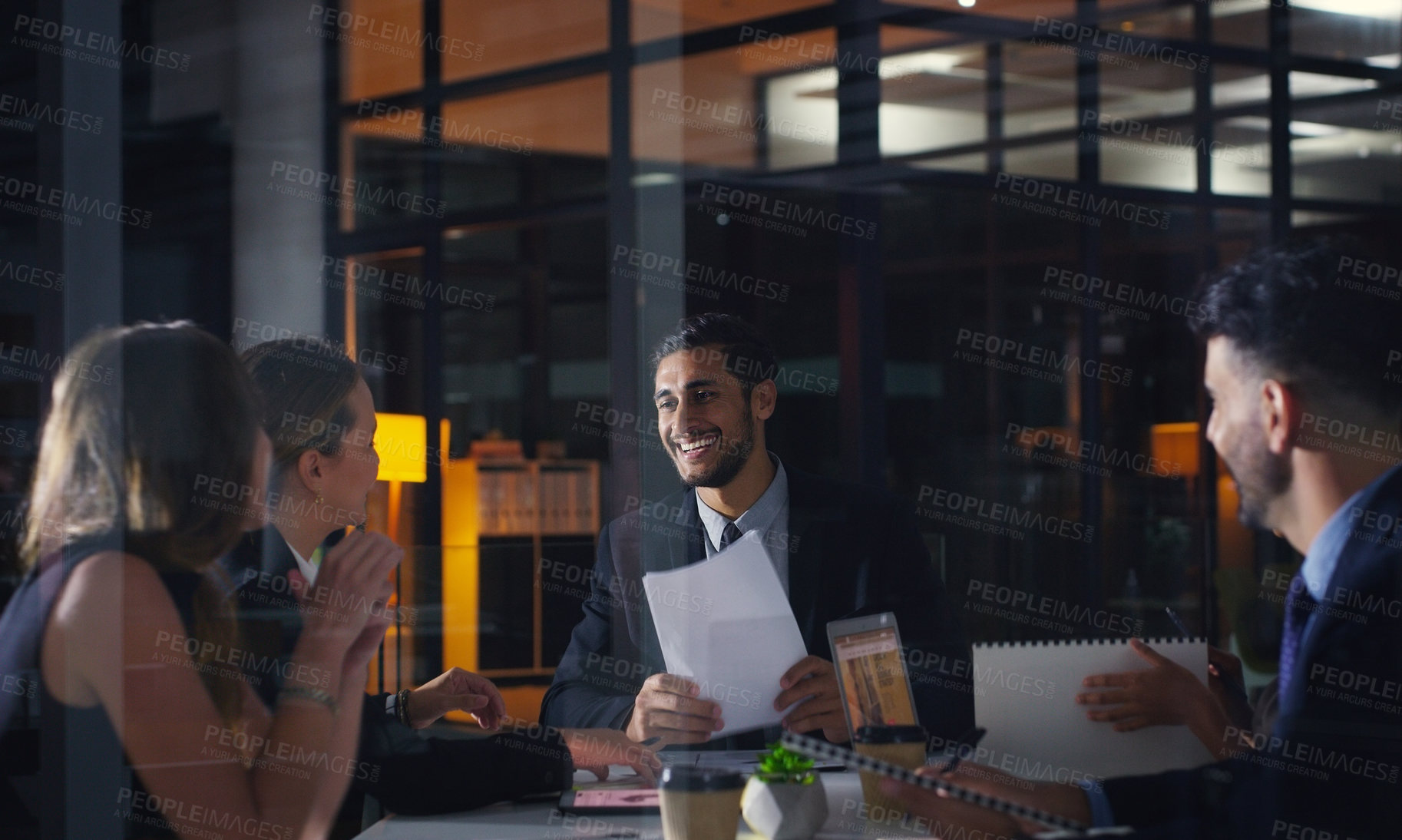 Buy stock photo Cropped shot of a diverse group of businesspeople sitting together and having a meeting in the office late at night