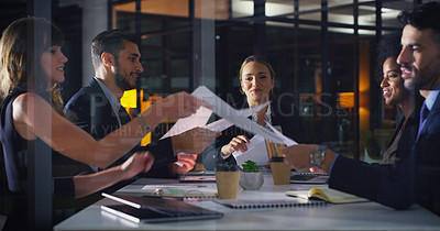 Buy stock photo Cropped shot of a diverse group of businesspeople sitting together and reading paperwork during a meeting late at night