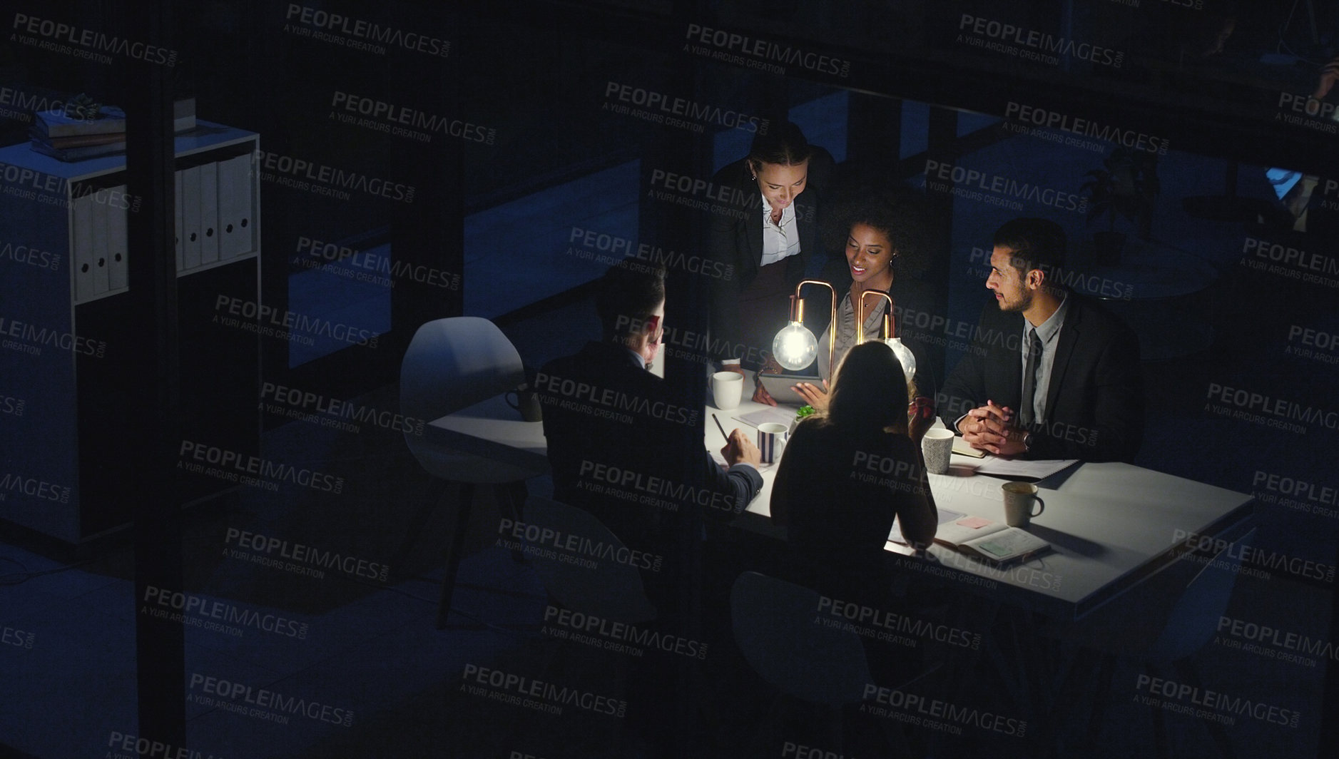 Buy stock photo Cropped shot of a diverse group of businesspeople sitting together and using a tablet during a meeting late at night