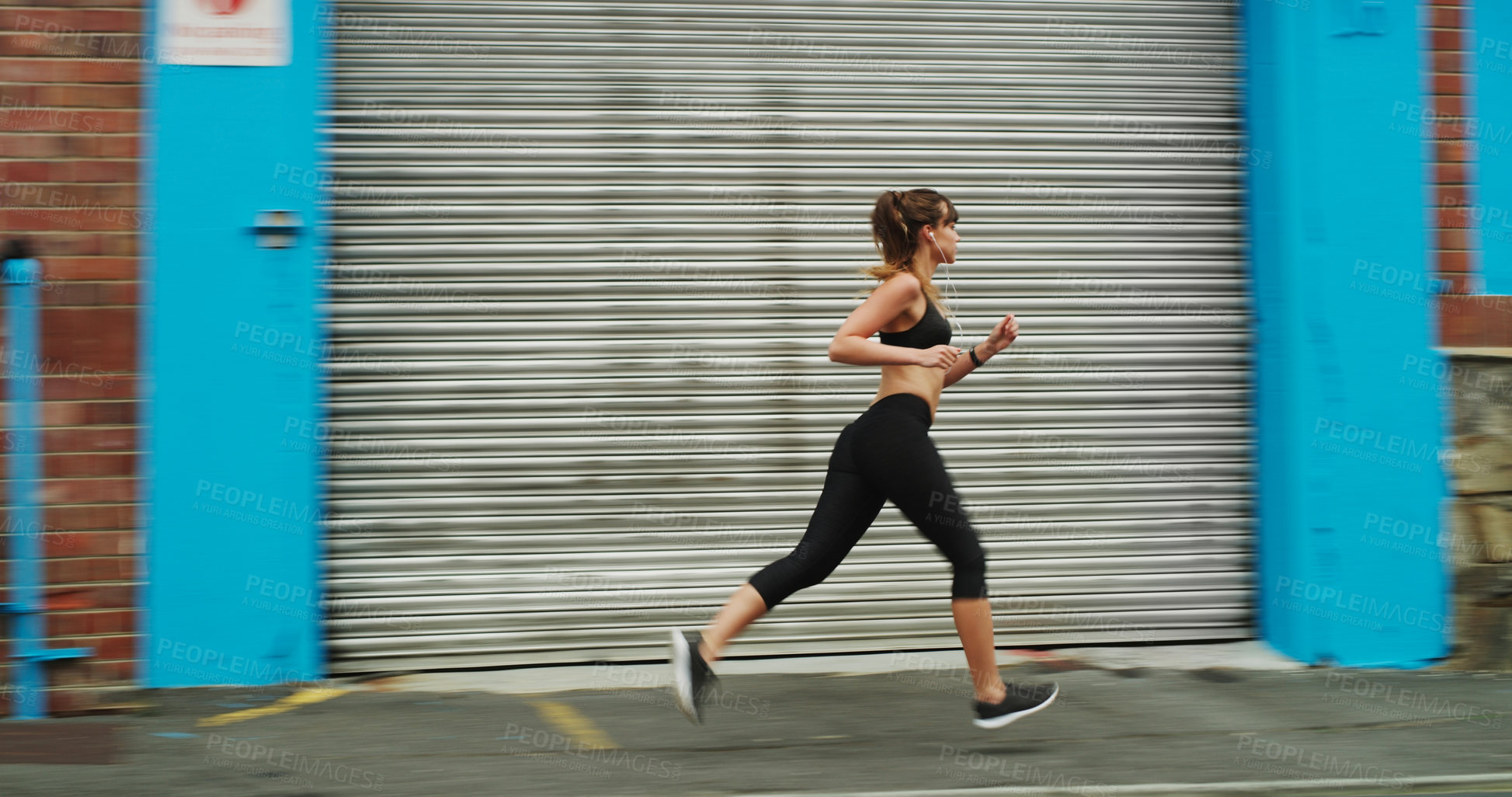 Buy stock photo Full length shot of an attractive young woman wearing gym wear and running down the street alone