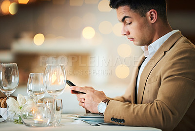 Buy stock photo Man, texting and phone at restaurant table for food, night and waiting for valentines day date. Young male, smartphone and wine glass for fine dining, bottle service or drink at dinner celebration