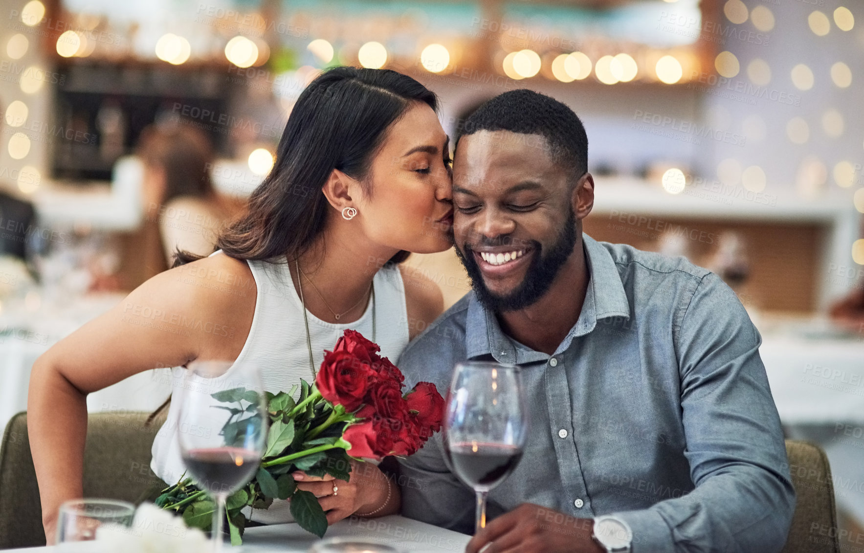 Buy stock photo Cropped shot of an affectionate  young woman kissing her boyfriend on his face in a restaurant