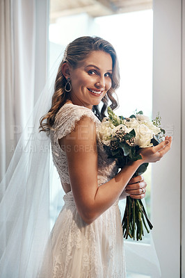 Buy stock photo Cropped portrait of an attractive young bride standing alone in the dressing room and holding her bouquet of flowers
