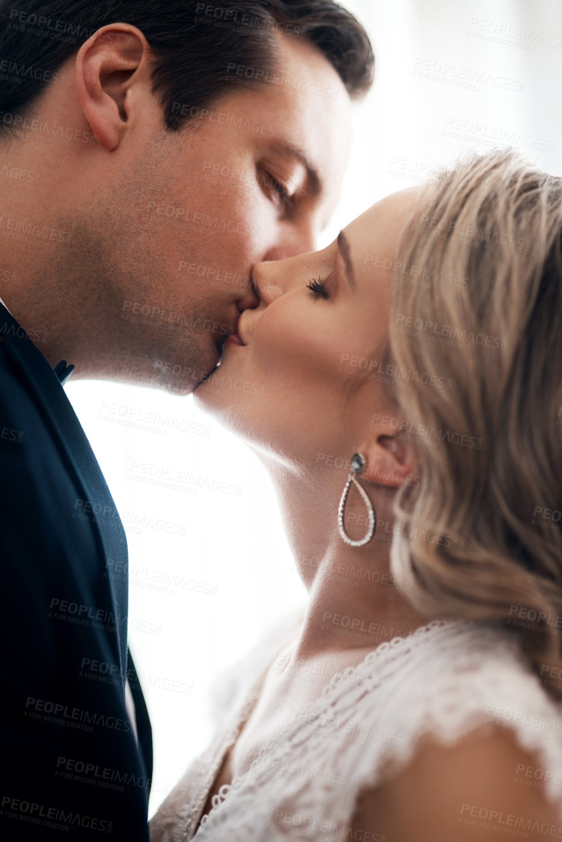 Buy stock photo Cropped shot of an affectionate young couple standing indoors together and kissing after their wedding
