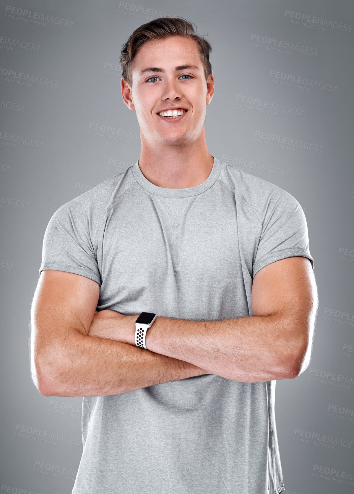 Buy stock photo Cropped portrait of a handsome young man standing alone against a gray studio background with his arms folded