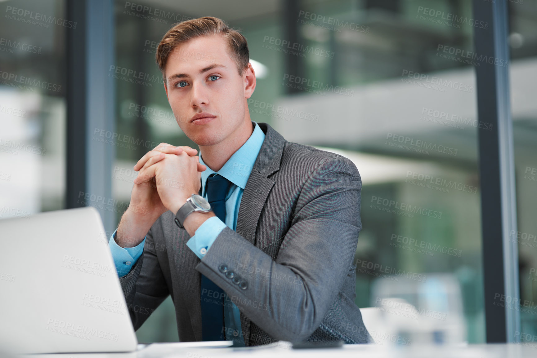 Buy stock photo Cropped portrait of a handsome young businessman sitting alone in his office and looking contemplative while using his laptop