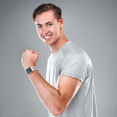 Buy stock photo Cropped portrait of a handsome young man standing alone against a gray studio background and flexing his bicep