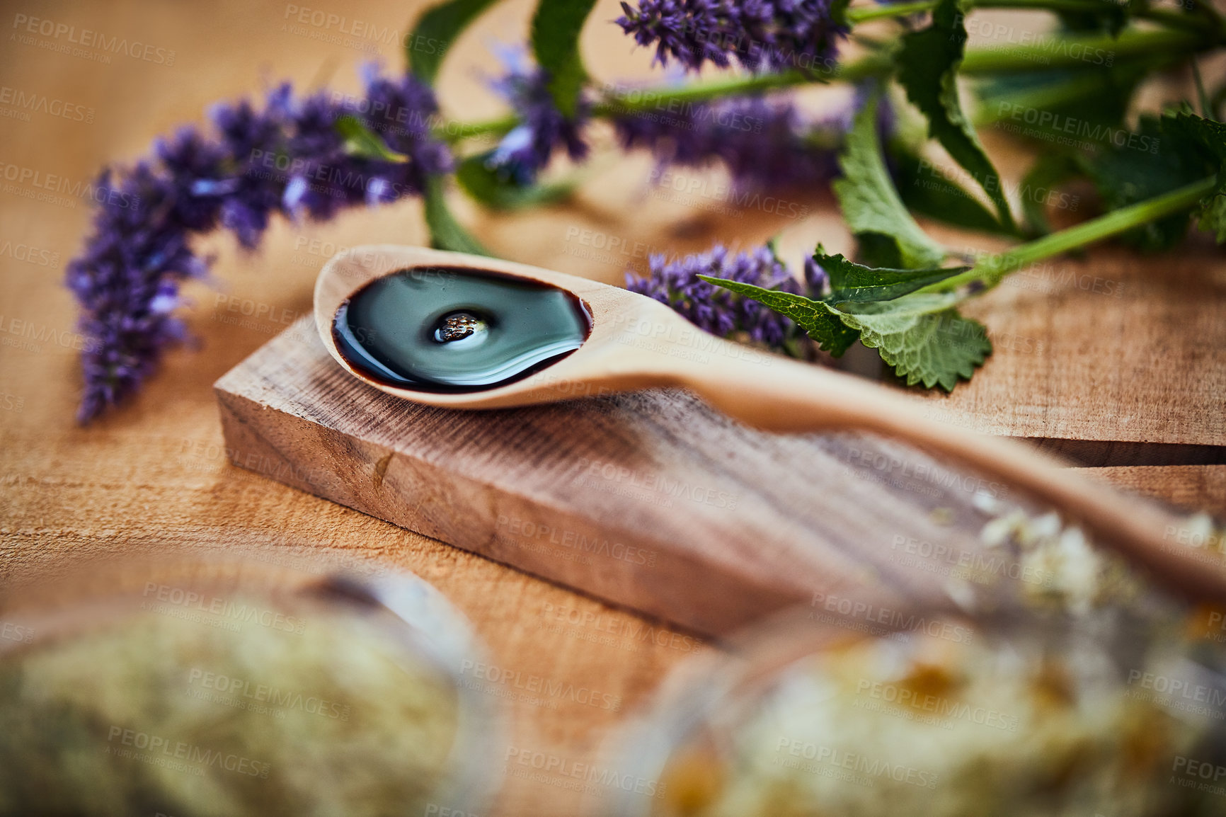 Buy stock photo Shot of a wooden spoon with dark liquid in it surrounded by fresh lavender on a table