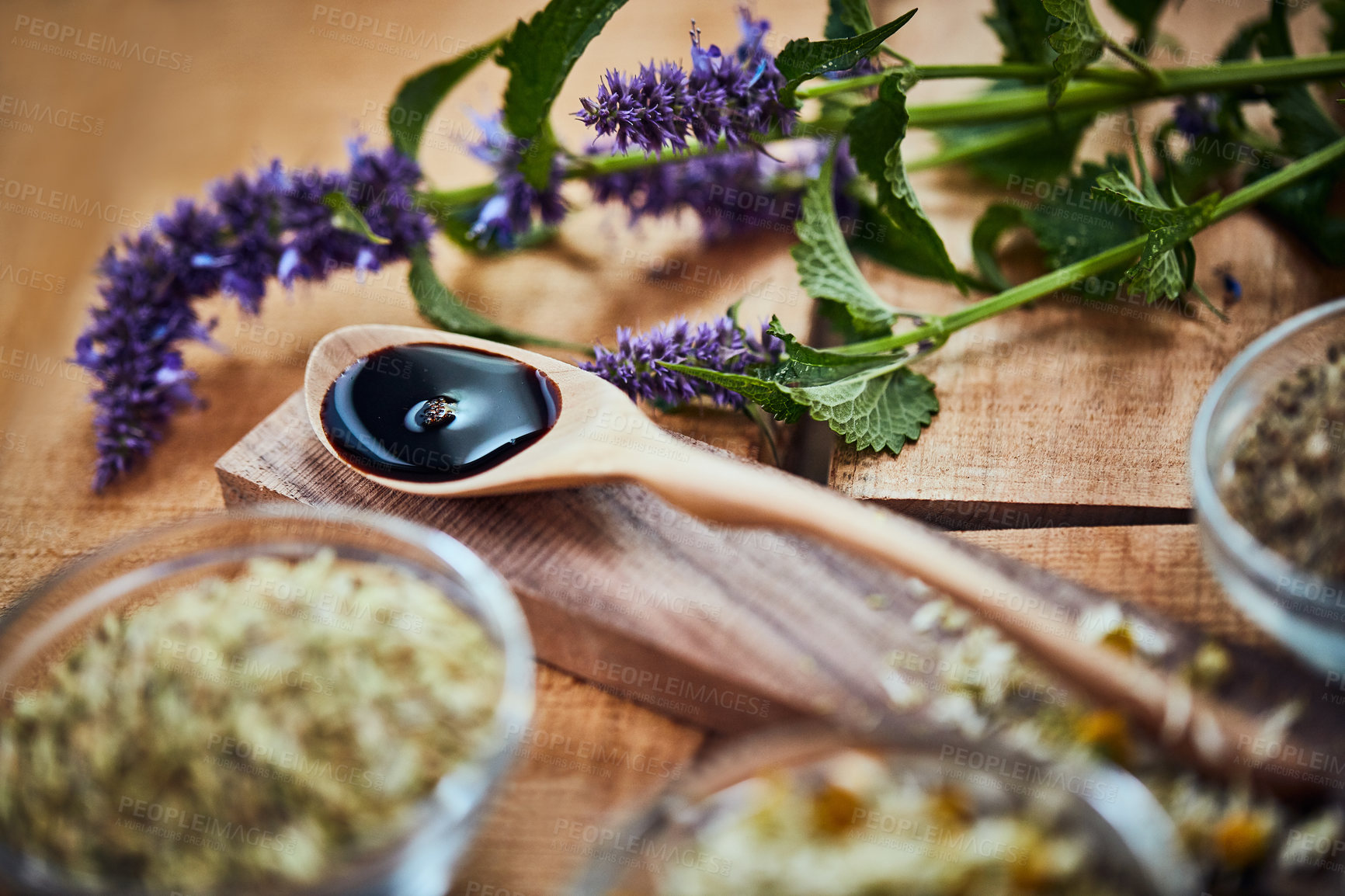 Buy stock photo Shot of a wooden spoon with dark liquid in it surrounded by fresh lavender on a table