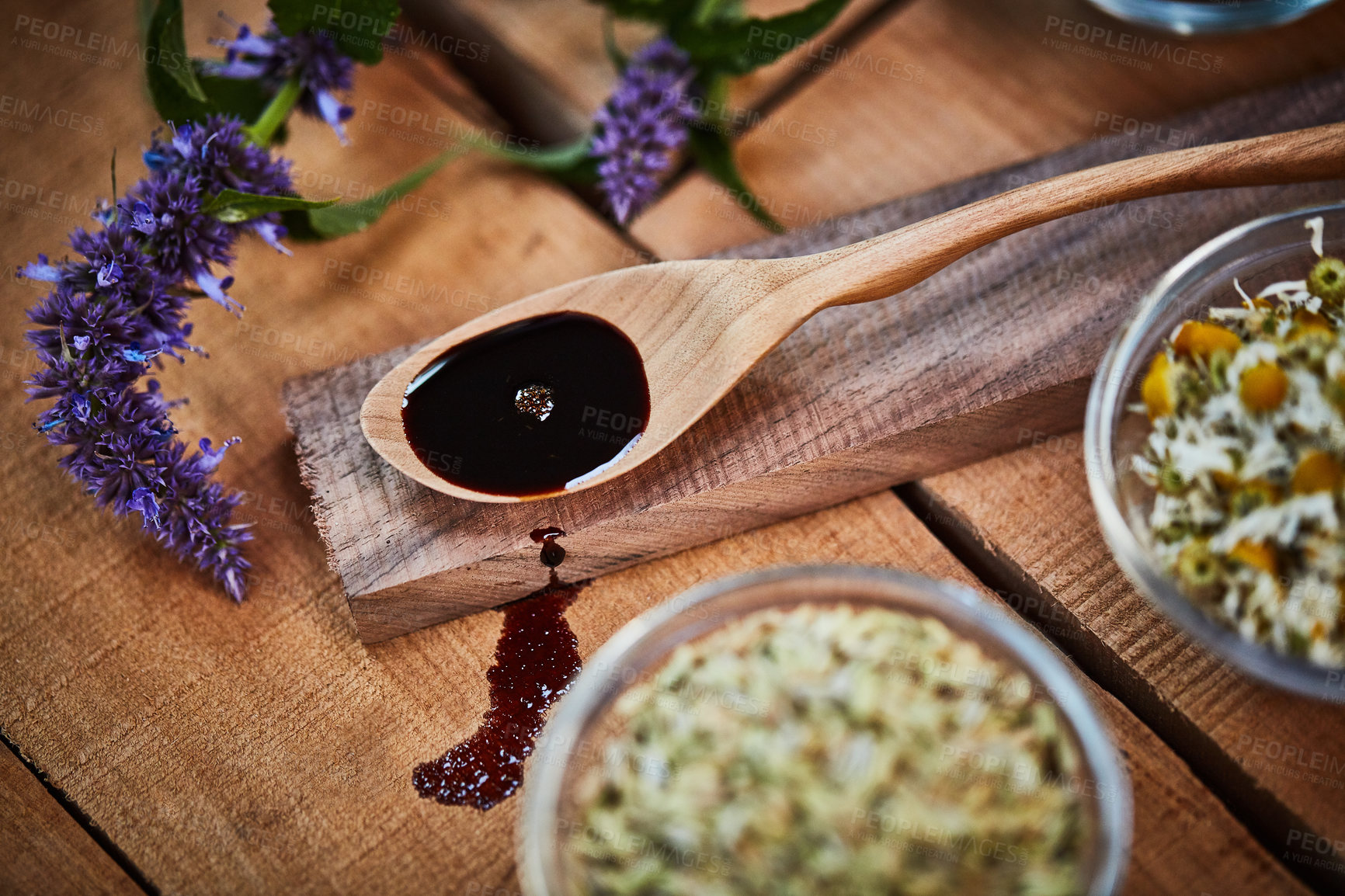 Buy stock photo Shot of a wooden spoon with dark liquid in it surrounded by fresh lavender on a table