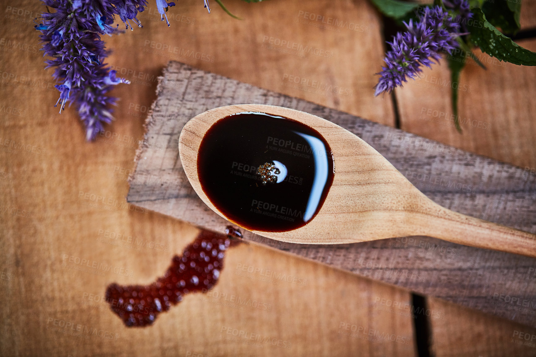 Buy stock photo Shot of a wooden spoon with dark liquid in it surrounded by fresh lavender on a table