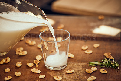 Buy stock photo Shot of a jug pouring of milk into a glass surrounded by nuts on a table