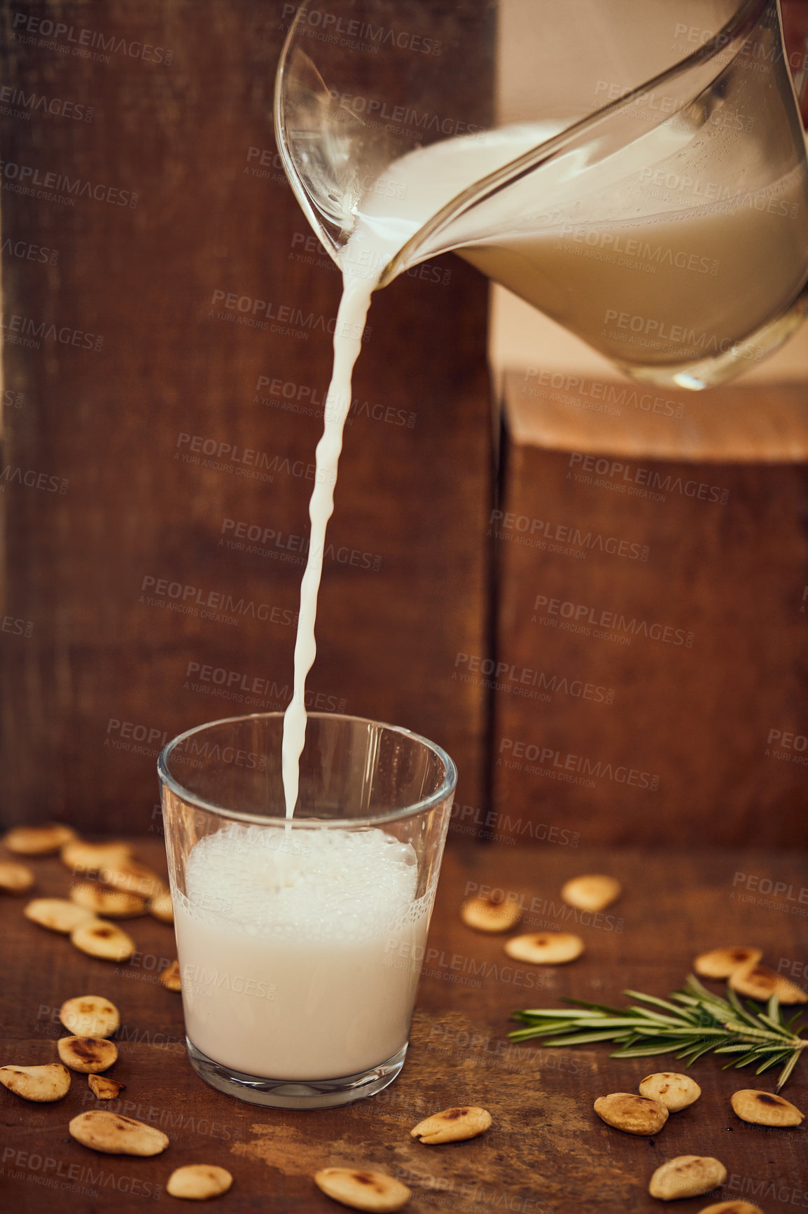 Buy stock photo Shot of a jug pouring of milk into a glass surrounded by nuts on a table