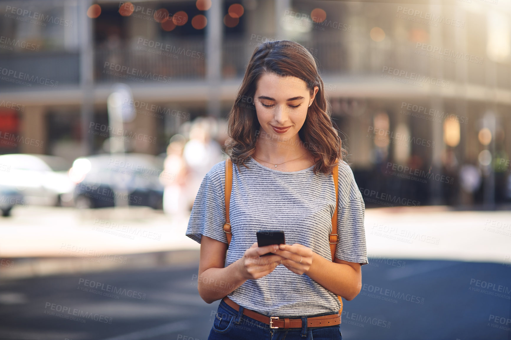Buy stock photo Cropped shot of an attractive young woman sending text messages while spending her day out in the city