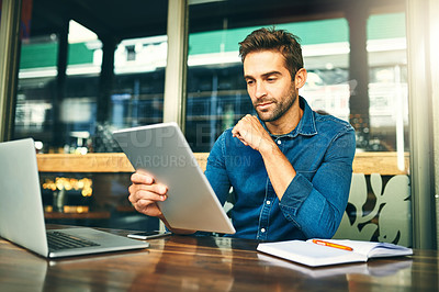 Buy stock photo Cropped shot of a handsome young businessman sitting alone and looking contemplative while using a tablet in a cafe