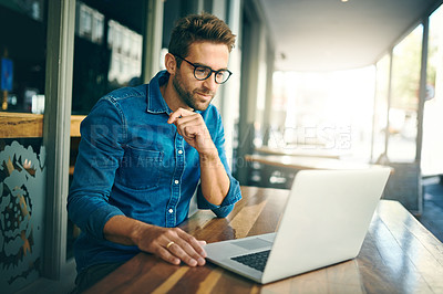 Buy stock photo Cropped shot of a handsome young businessman sitting alone and looking contemplative while using his laptop in a cafe