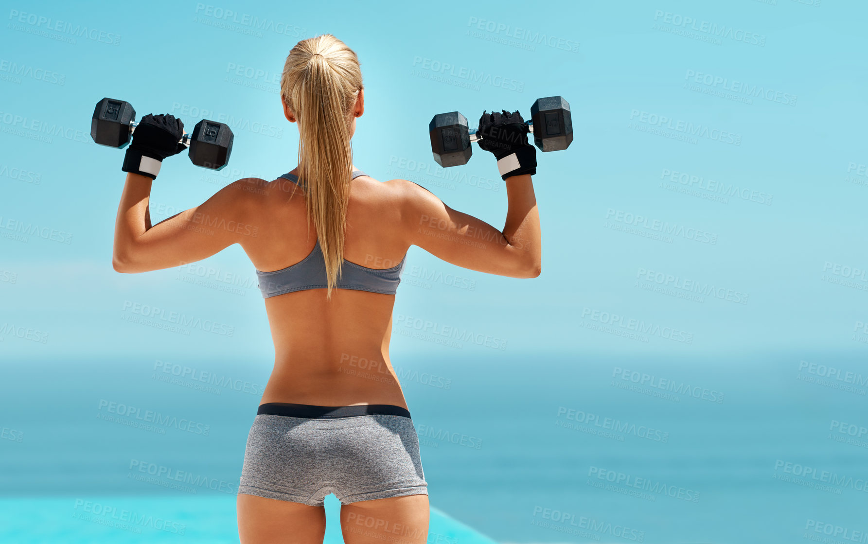 Buy stock photo Rearview shot of an unrecognizable young woman exercising with dumbbells outdoors