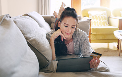 Buy stock photo Full length shot of an attractive young woman looking thoughtful while using a digital tablet and a credit card to shop online in her living room