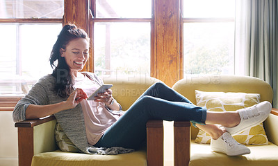 Buy stock photo Full length shot of an attractive young woman smiling while using a smartphone on her couch at home