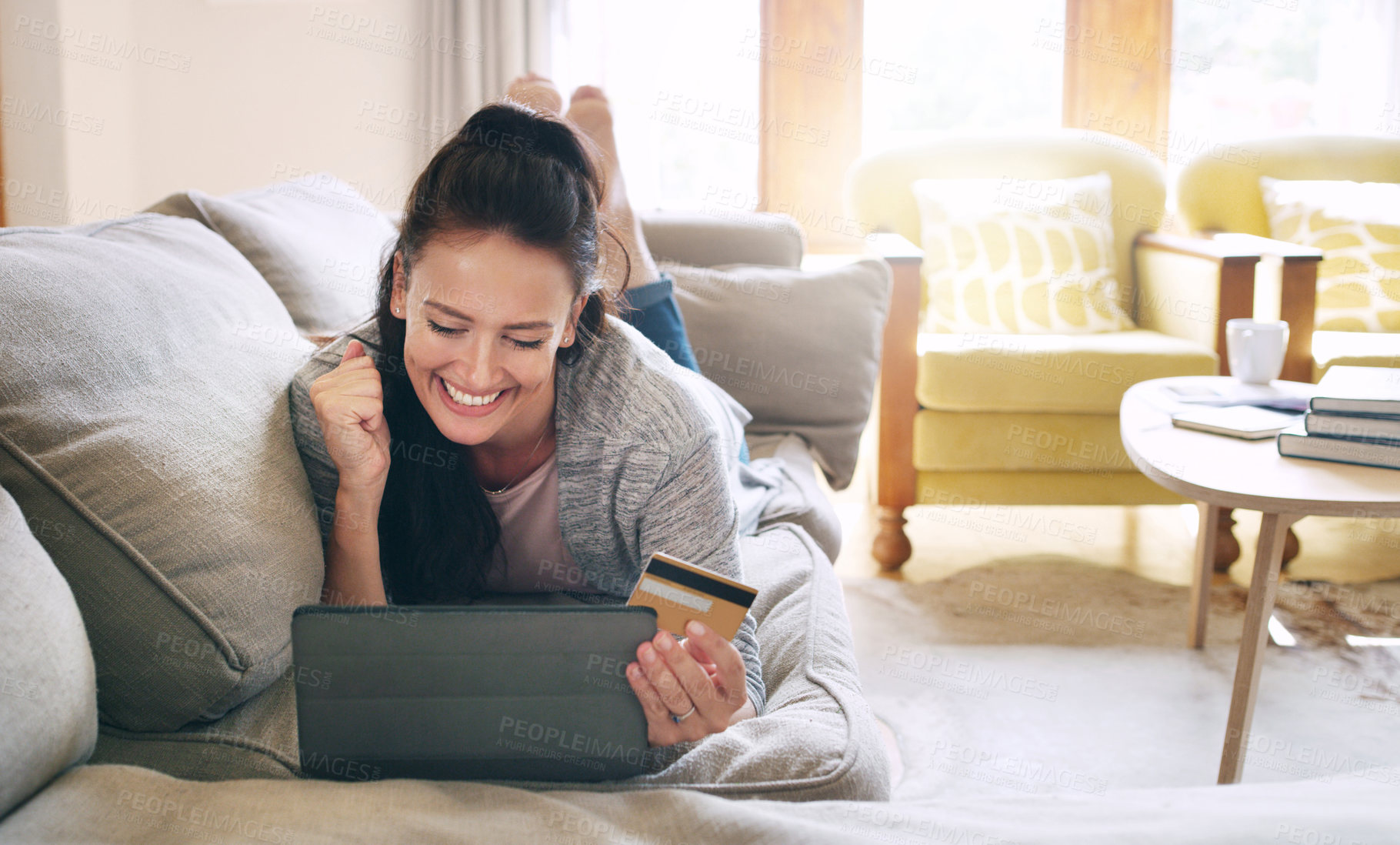 Buy stock photo Full length shot of an attractive young woman cheering while holding a digital tablet and a credit card on her couch at home