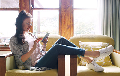 Buy stock photo Full length shot of an attractive young woman using a smartphone while relaxing on her couch at home