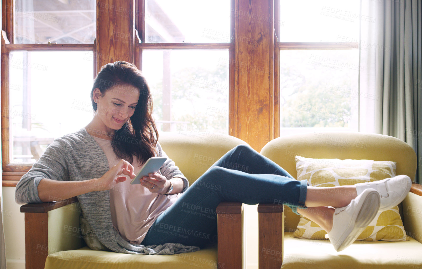 Buy stock photo Full length shot of an attractive young woman using a smartphone while relaxing on her couch at home