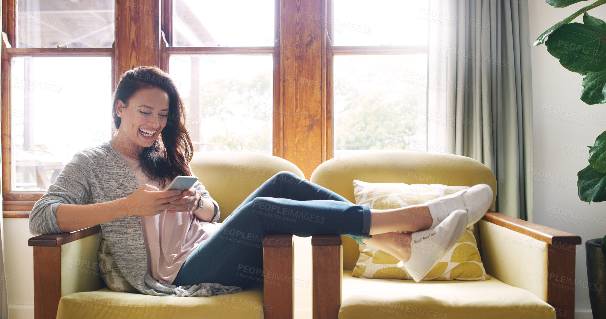 Buy stock photo Full length shot of an attractive young woman laughing while using a smartphone on her couch at home