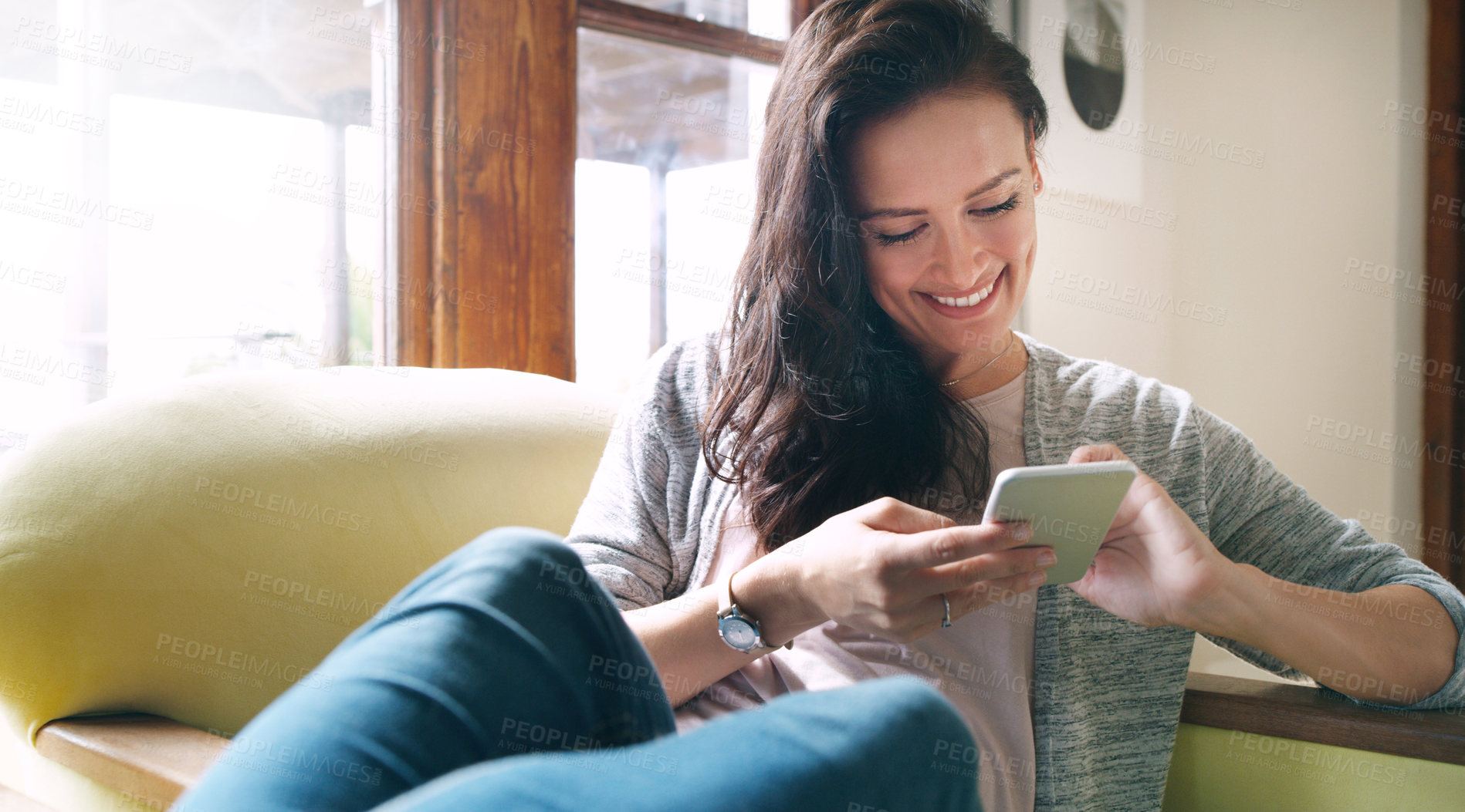 Buy stock photo Cropped shot of an attractive young woman smiling while using a smartphone on her couch at home