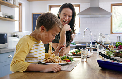 Buy stock photo Cropped shot of an affectionate young boy going in on his spaghetti while his mother laughs in the background