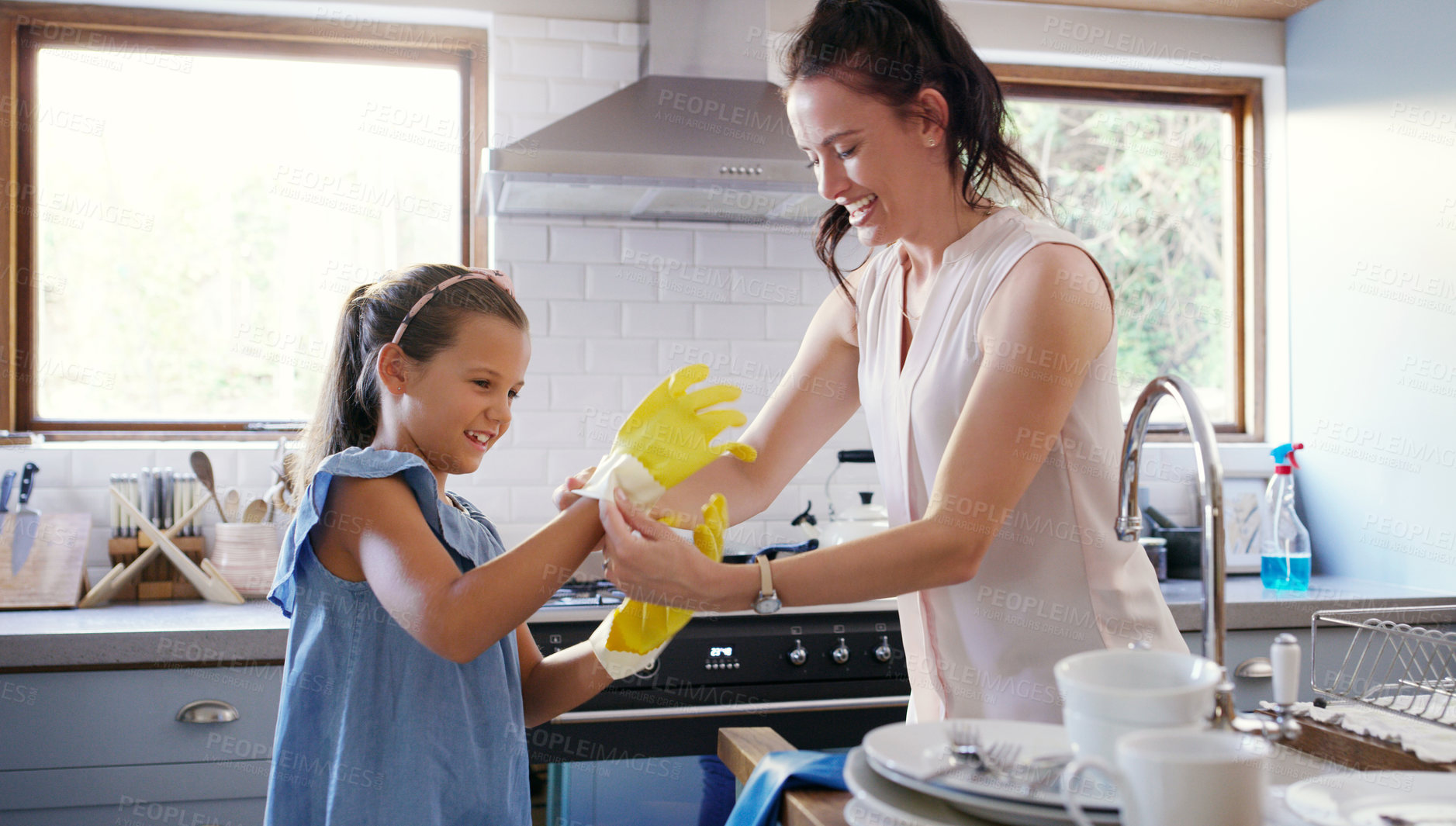 Buy stock photo Cropped shot of an affectionate young mother helping  her daughter to put on rubber gloves while doing the dishes at home