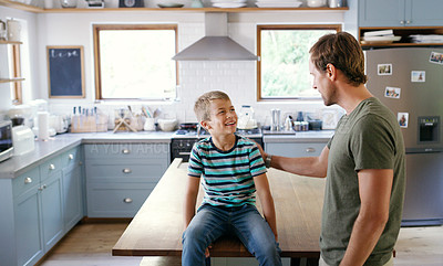 Buy stock photo Cropped shot of an affectionate young boy looking at his father while sitting on the kitchen counter at home