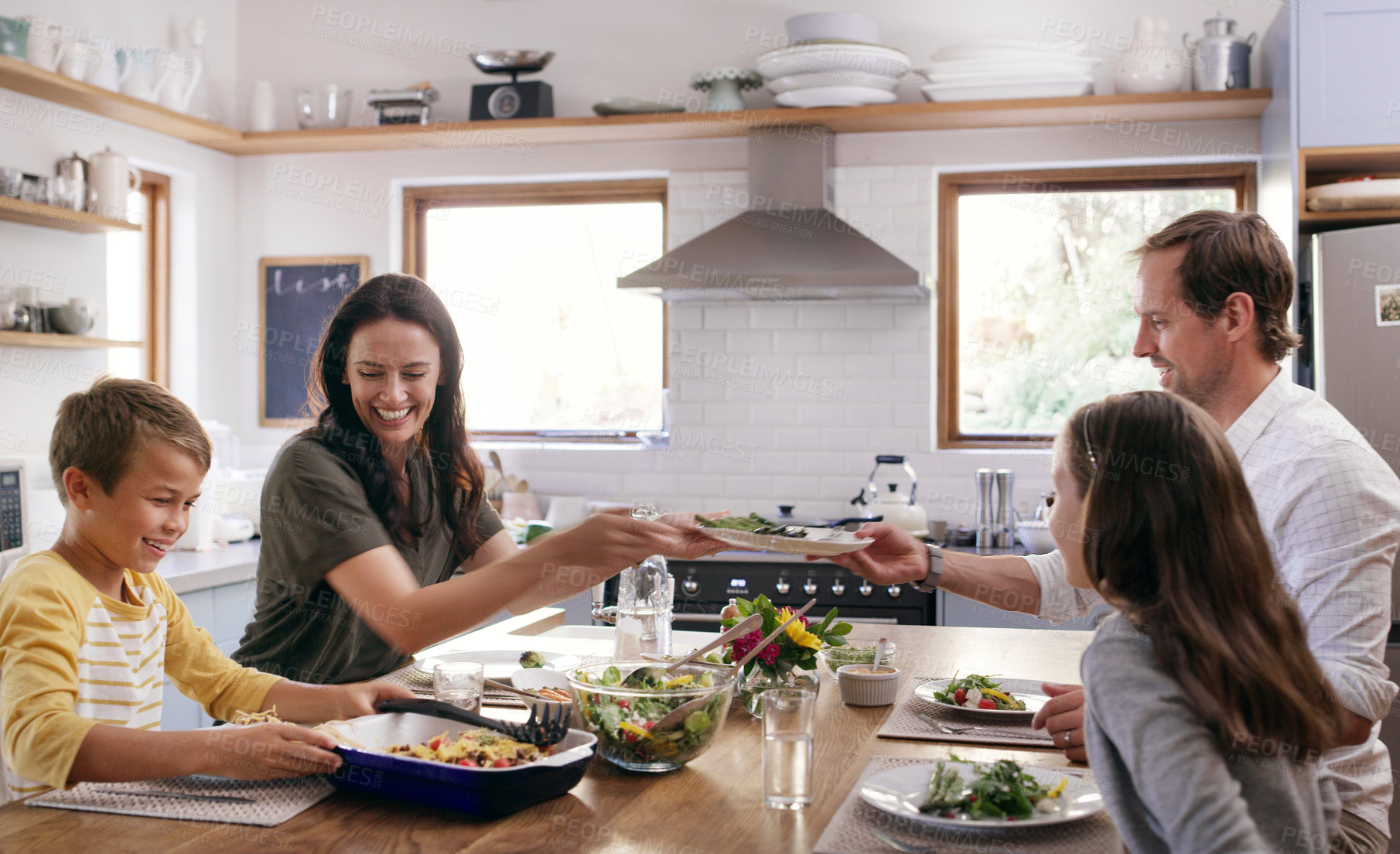 Buy stock photo Cropped shot of two affectionate young parents having a meal with their kids in the kitchen at home
